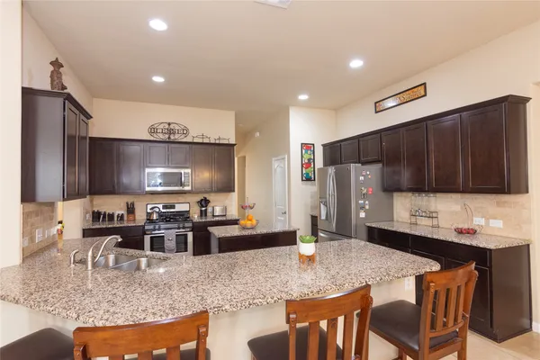 a kitchen with stainless steel appliances granite countertop a stove top oven a sink a dining table and chairs