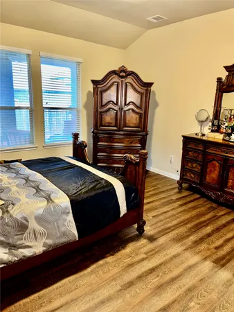 a bedroom with a bed and dresser with wooden floor