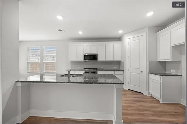 a kitchen with stainless steel appliances granite countertop a refrigerator a sink dishwasher a stove and white countertops with wooden floor