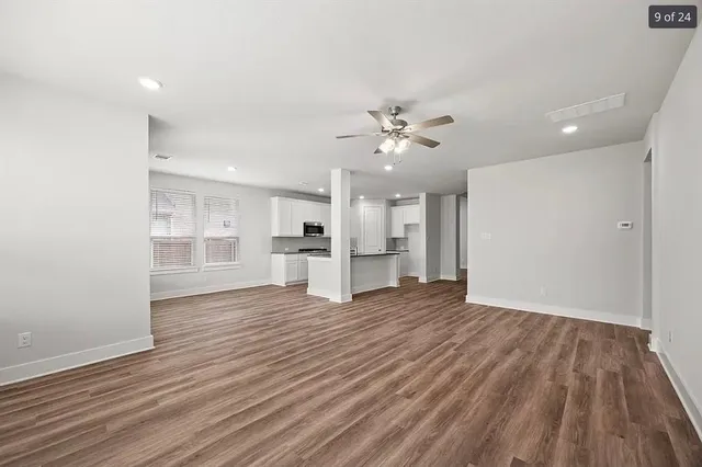 a view of empty room with wooden floor and kitchen