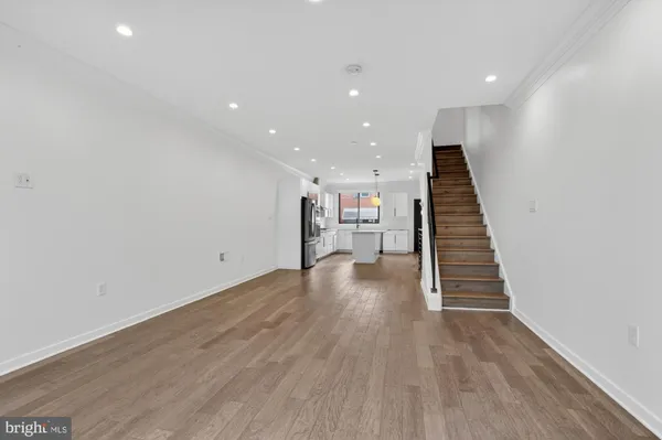 an empty room with wooden floor staircase and a living room