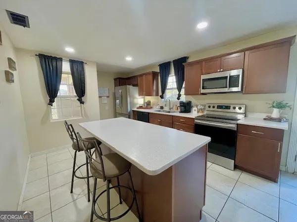 a kitchen with stainless steel appliances kitchen island granite countertop a sink a stove a refrigerator cabinets and chairs