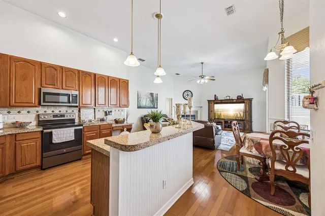 a kitchen with kitchen island granite countertop wooden floors a stove top oven a sink dishwasher a dining table and chairs with wooden floor