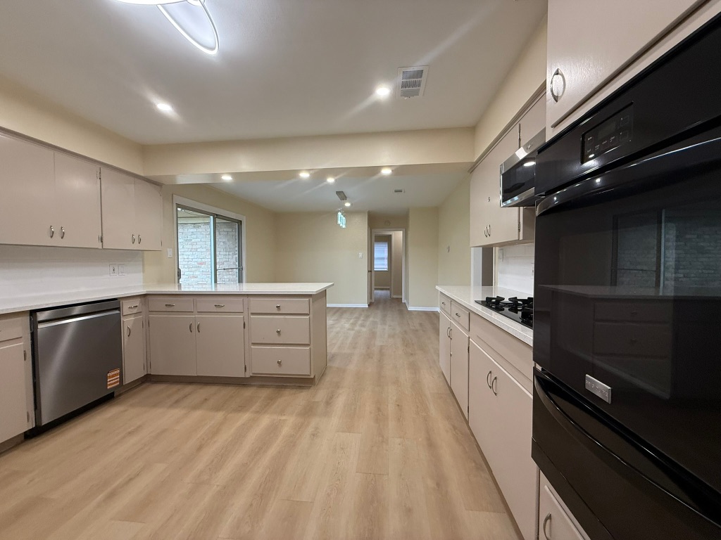 4603 Roundup Trail Austin, TX 78745 - Photo 11 of 35 Kitchen with black appliances, a peninsula, light countertops, a warming drawer, and light wood-type flooring
