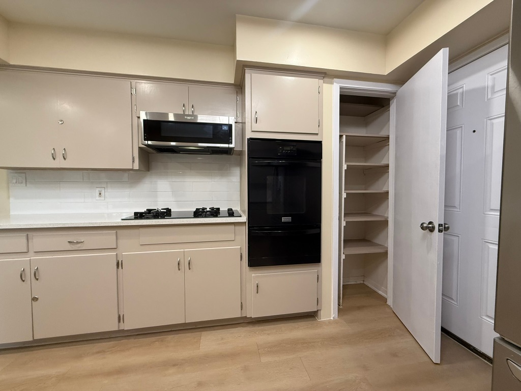 4603 Roundup Trail Austin, TX 78745 - Photo 13 of 35 Kitchen with black appliances, a warming drawer, light wood finished floors, and backsplash