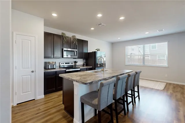 a kitchen with stainless steel appliances granite countertop a stove a refrigerator a sink dishwasher a dining table and chairs with wooden floor