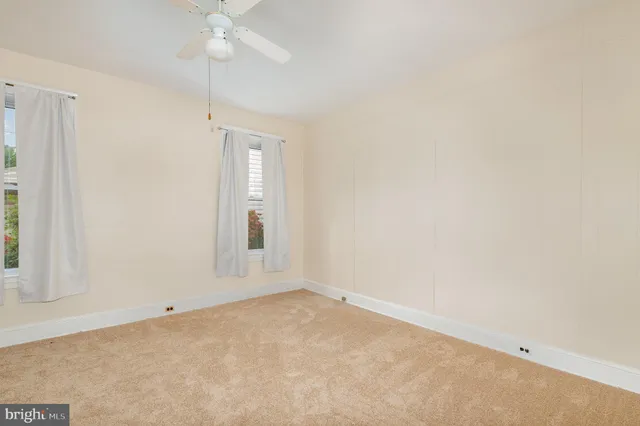 an empty room with a chandelier fan and windows