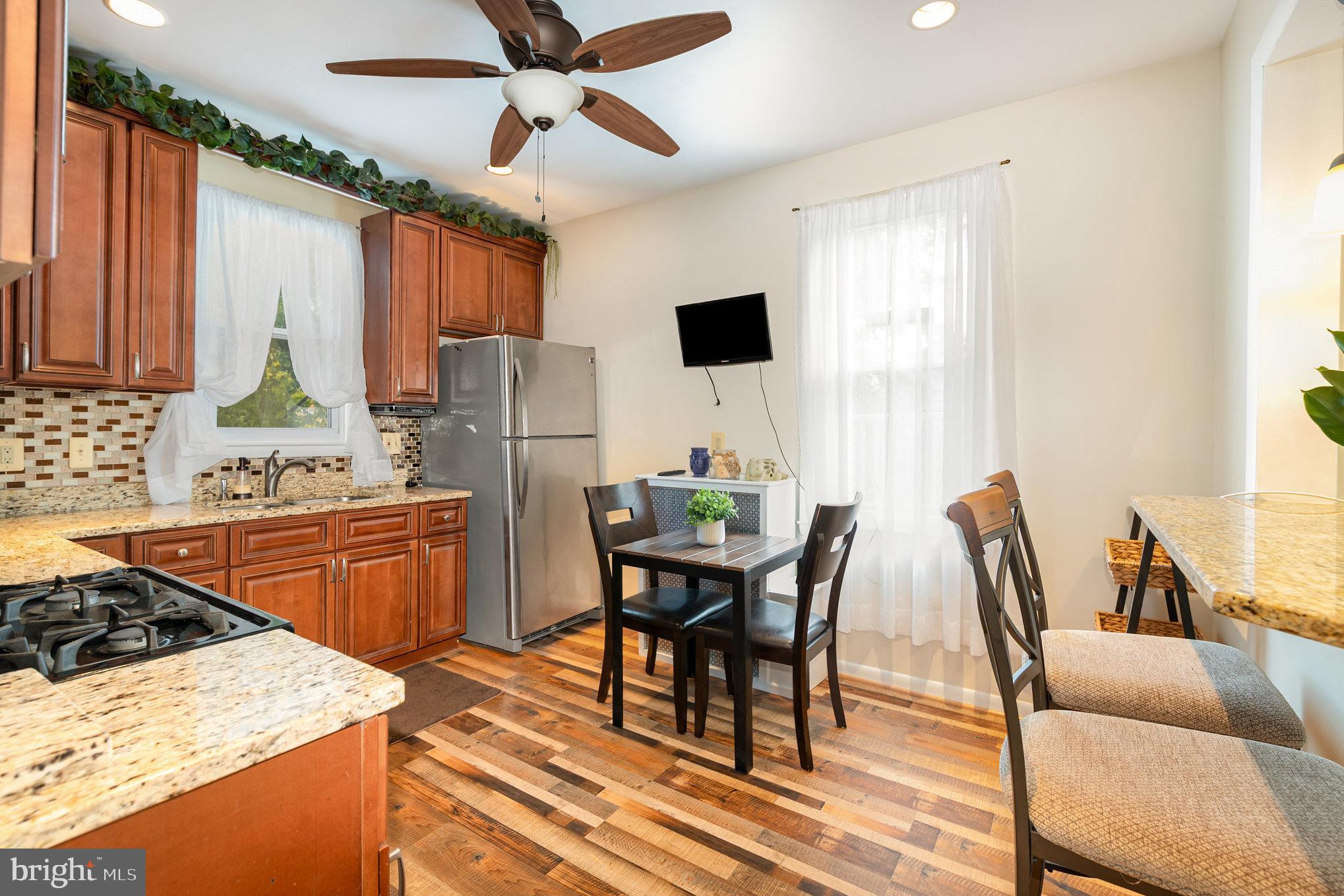 5005 Catalpha Road Baltimore, MD 21214 - Photo 17 of 31 a kitchen with stainless steel appliances granite countertop a stove a sink a microwave a dining table and chairs with wooden floor