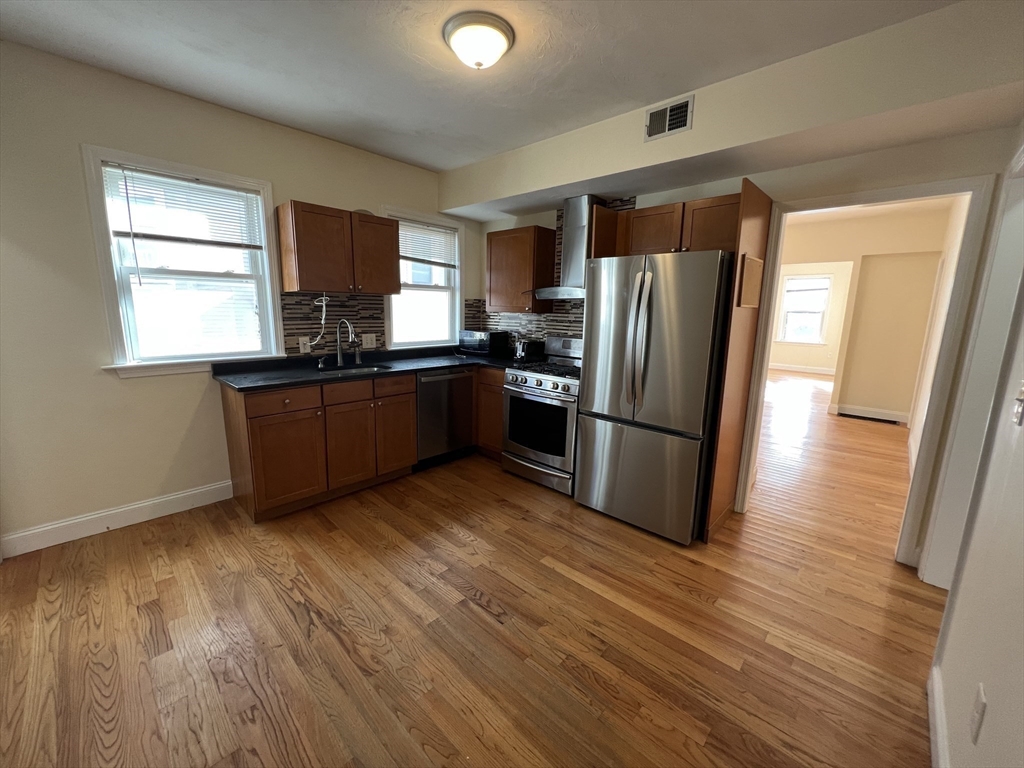 12 Weld Hill Street, Unit 2 Boston, MA 02130 - Photo 4 of 9 a kitchen with stainless steel appliances granite countertop a refrigerator microwave and stove with wooden floor