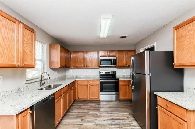 a kitchen with stainless steel appliances granite countertop a refrigerator a sink dishwasher a stove top oven and a dining table with wooden floor