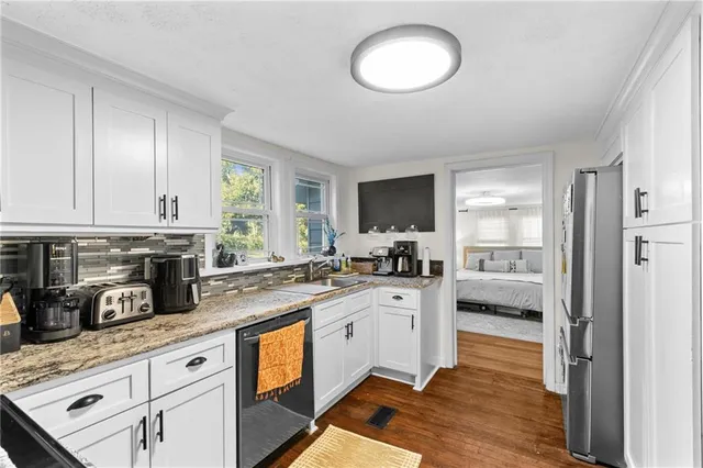 a kitchen with stainless steel appliances granite countertop a stove top oven a sink dishwasher a refrigerator and a dining table with wooden floor