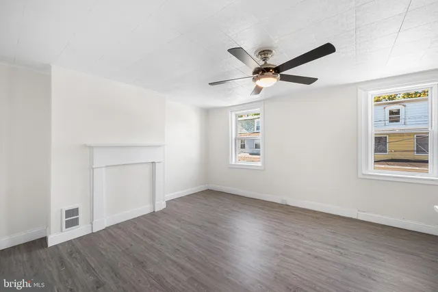an empty room with wooden floor a ceiling fan and windows