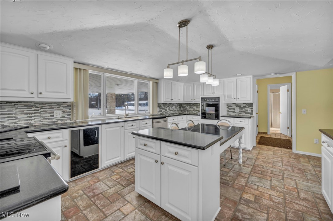 36350 Bainbridge Road Solon, OH 44139 - Photo 10 of 38 Kitchen featuring a center island, sink, decorative backsplash, decorative light fixtures, and white cabinetry