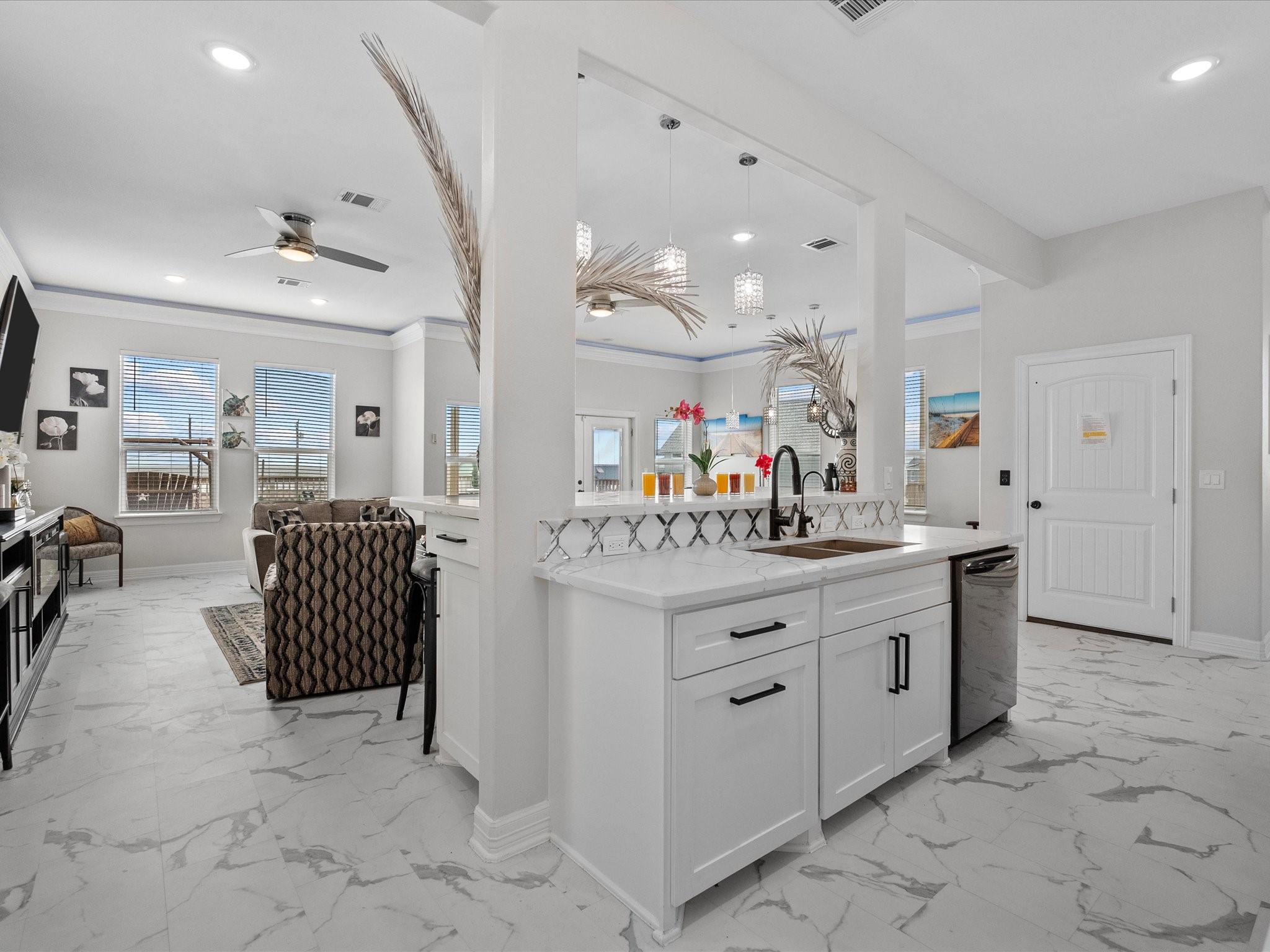 1018 Seashell Drive Surfside Beach, TX 77541 - Photo 16 of 49 This photo showcases a modern open-concept living space with a bright kitchen featuring white cabinetry, sleek countertops, and pendant lighting. The adjacent living area has large windows, a ceiling fan, and stylish furnishings, creating a welcoming and airy atmosphere.