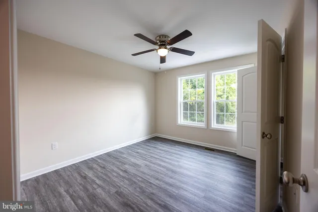 an empty room with wooden floor a ceiling fan and windows