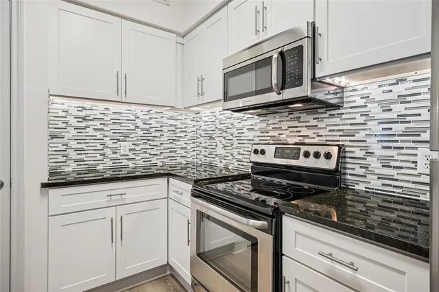a kitchen with stainless steel appliances granite countertop white cabinets granite counter tops and a wooden floor