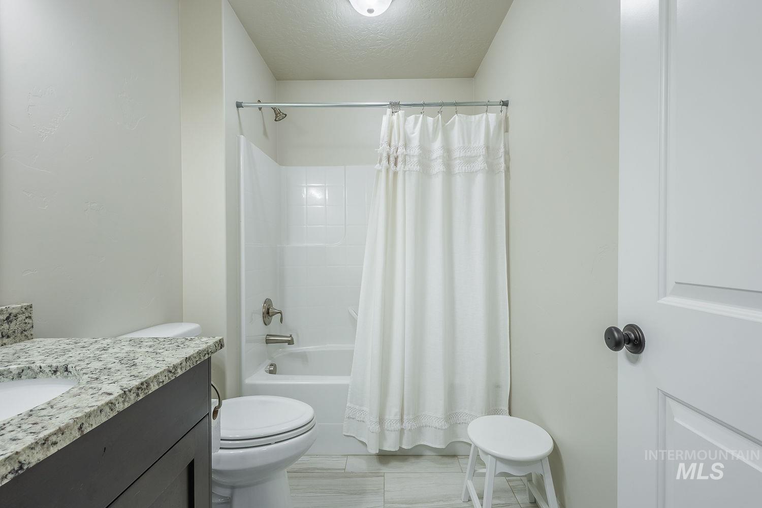 8077 Star Pass Ridge Road Nampa, ID 83686 - Photo 32 of 37 Full bathroom featuring a tub/shower combination with a white surround, a dark wood-finish vanity with a light-toned countertop, and light-toned floor tiling