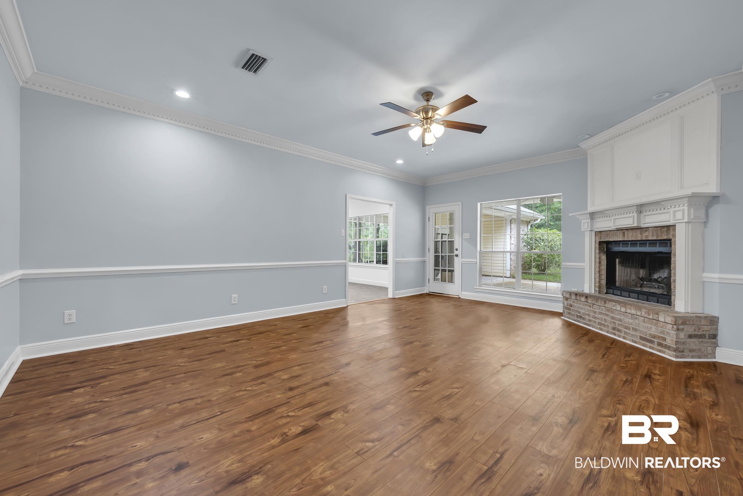 14960 Howells Ferry Road Wilmer, AL 36587 - Photo 7 of 22 Spacious living area featuring rich wood-finish flooring, a brick fireplace with a detailed white mantel, and extensive crown molding