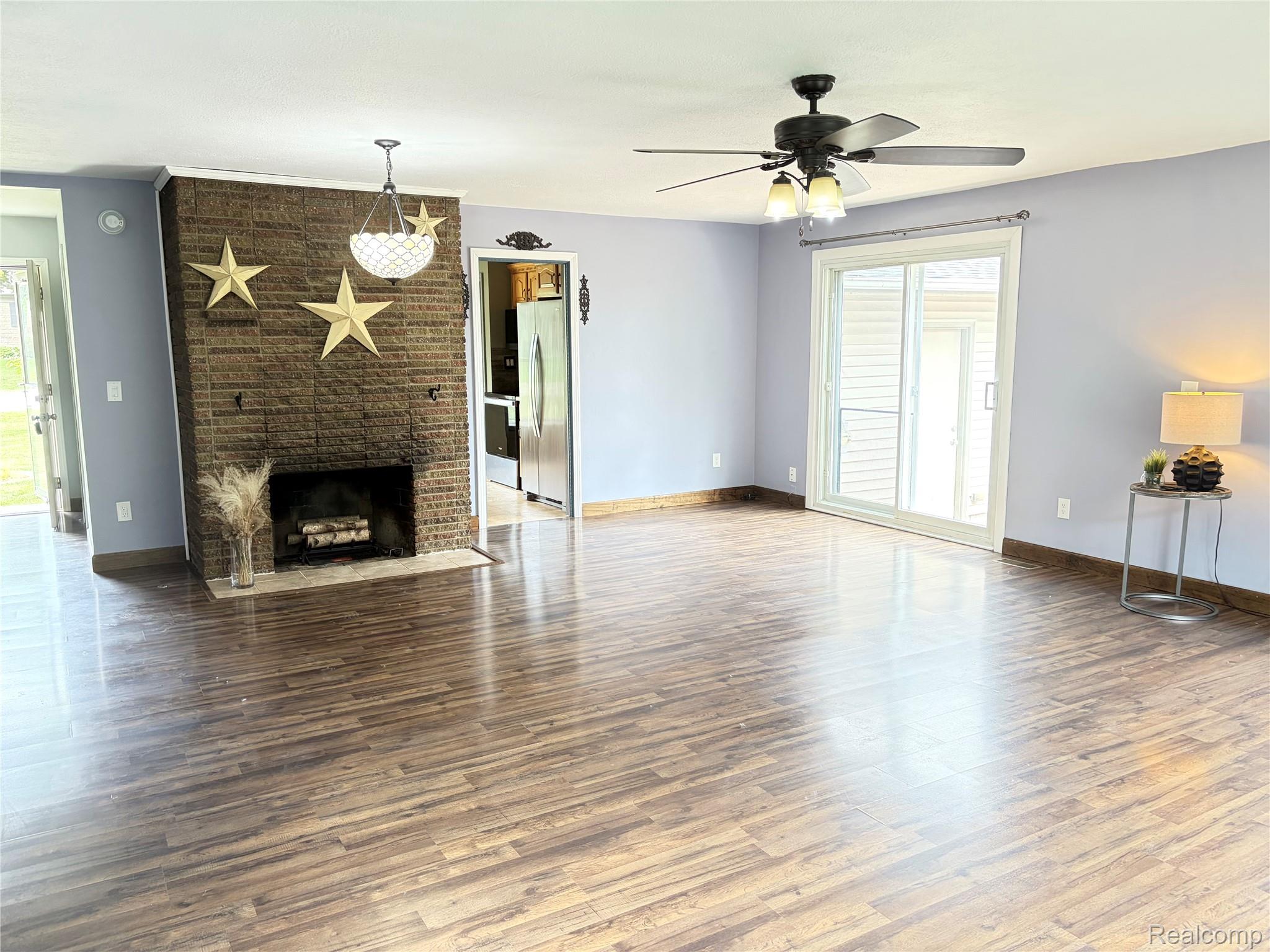 1451 Wilshire Road Haslett, MI 48840 - Photo 13 of 42 Spacious room featuring wood-finish flooring, a brick fireplace with a hearth, a ceiling fan with light fixture, and a sliding glass door