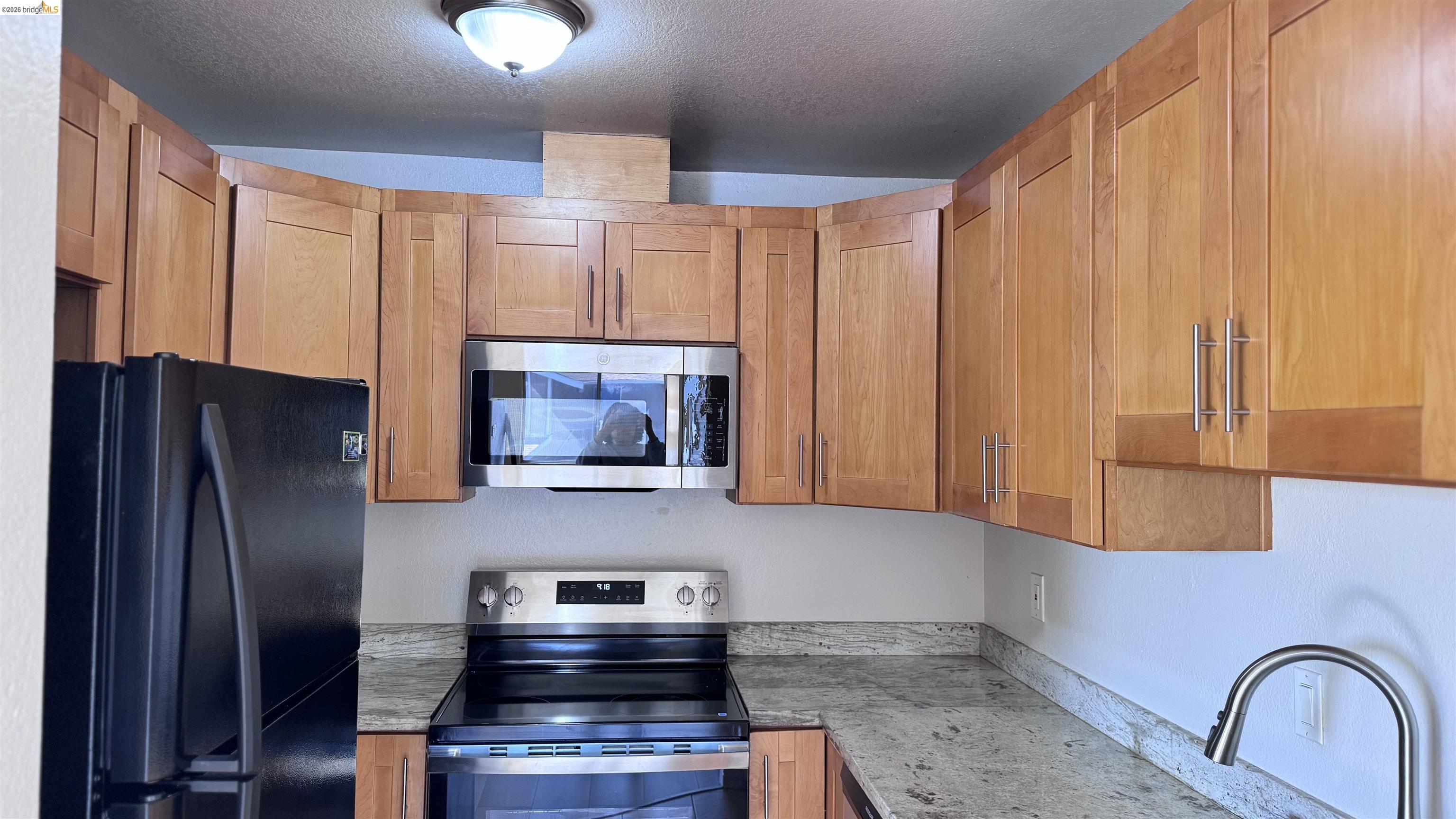 23 Raintree Court, Unit 15 Hayward, CA 94544 - Photo 2 of 16 Kitchen with stainless steel appliances, wood finish cabinets, a textured ceiling, and light stone countertops