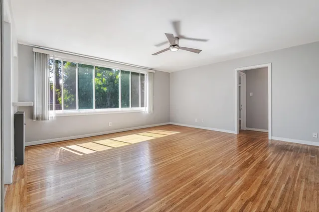 a view of empty room with wooden floor and fan