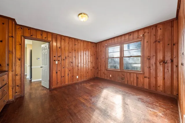 an empty room with wooden floor and windows with curtains