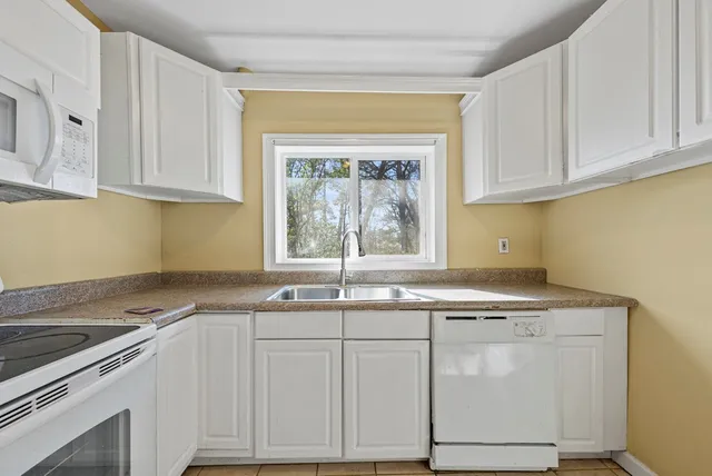 a kitchen with granite countertop a sink stainless steel appliances white cabinets and a window