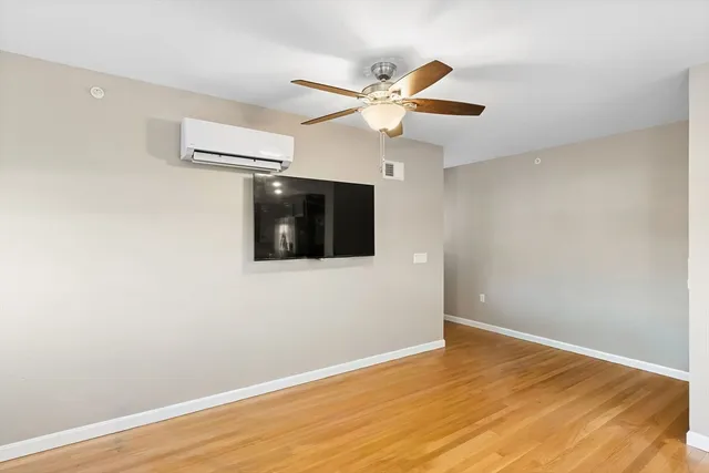 a view of an empty room with wooden floor and a ceiling fan