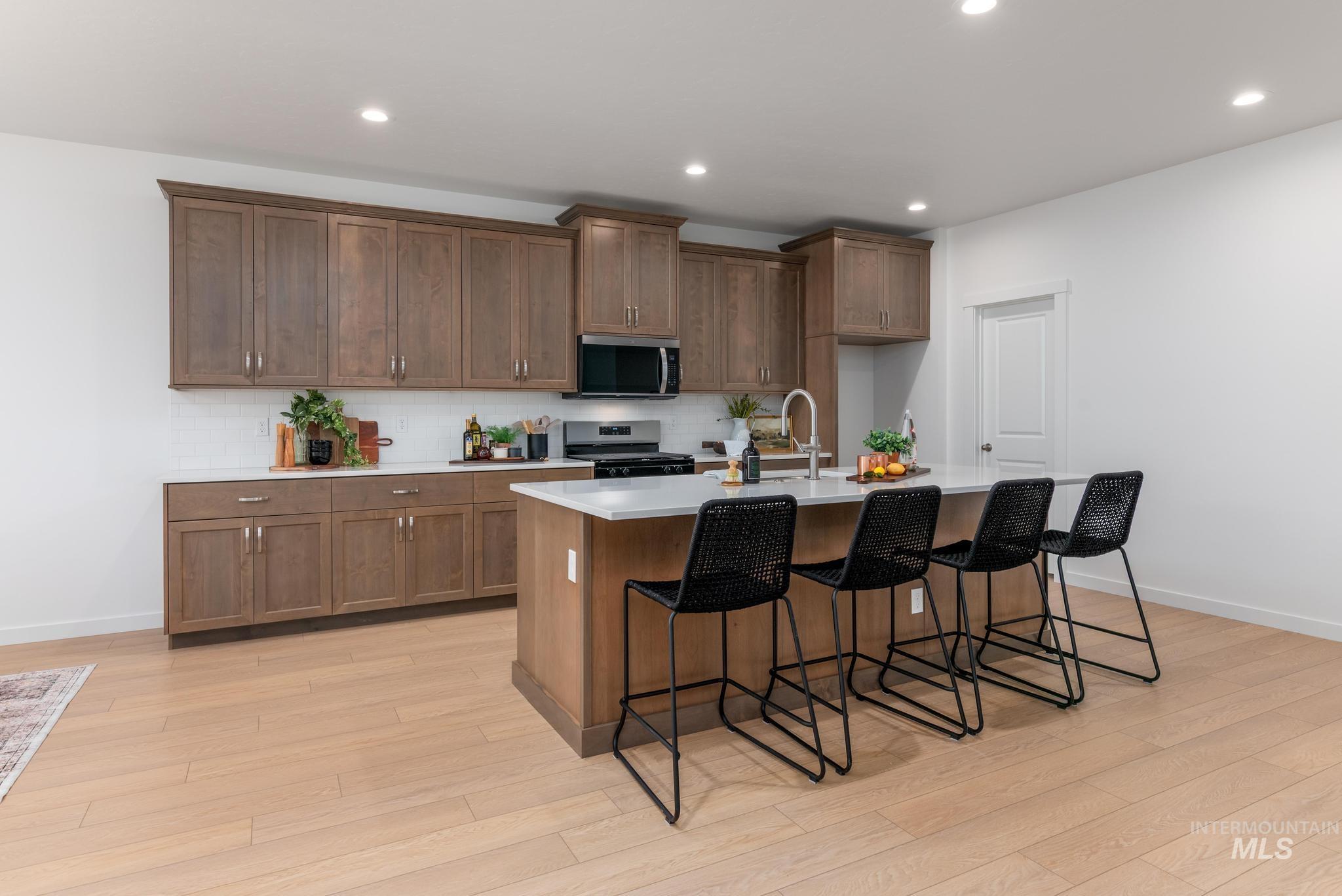 6285 West Snow Currant Street Meridian, ID 83646 - Photo 5 of 10 Kitchen with stainless steel appliances, a kitchen bar, a center island with sink, brown cabinets, and light wood-type flooring