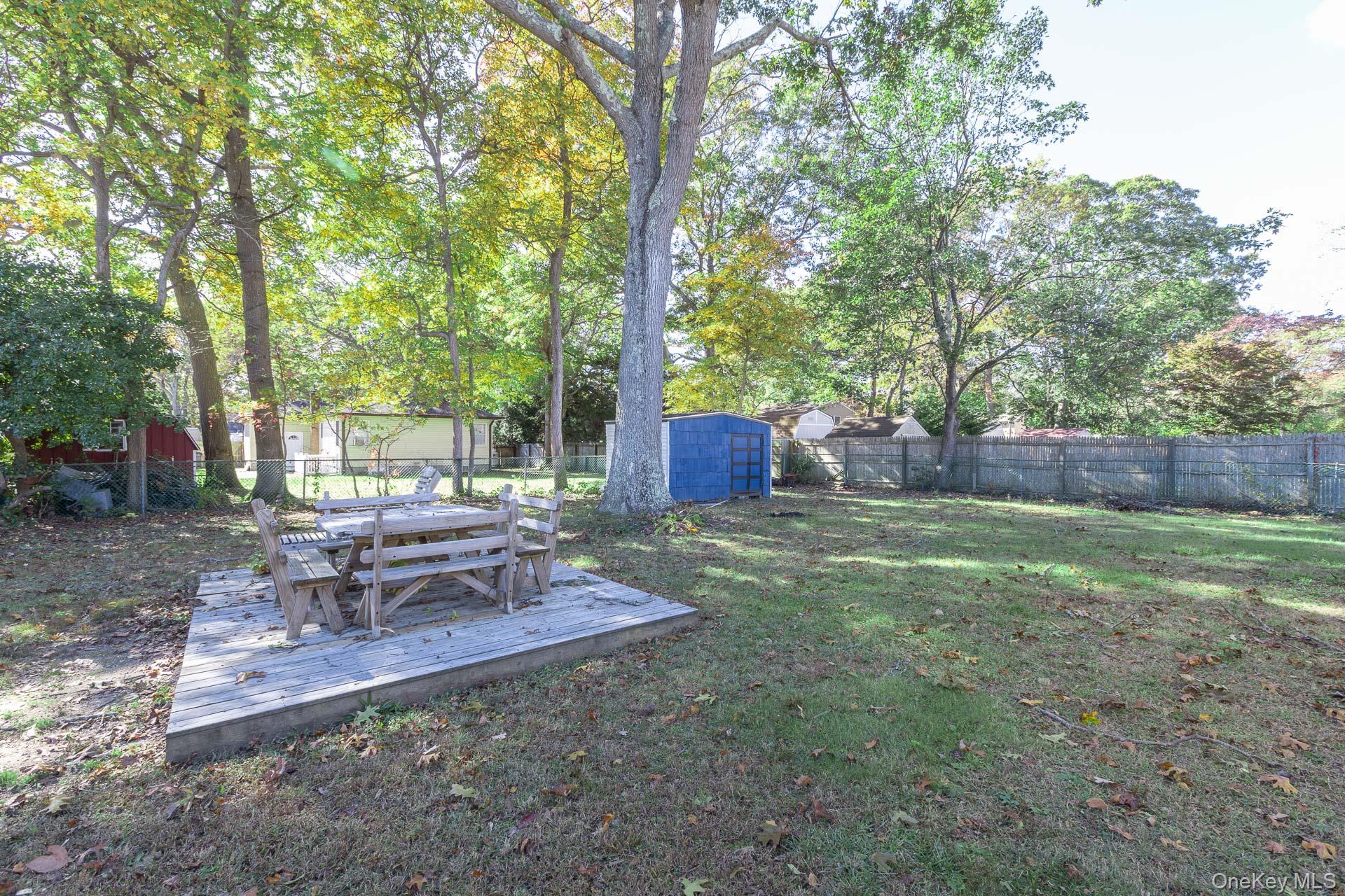 12 Applegate Drive Mastic, NY 11950 - Photo 25 of 29 Fenced backyard with outdoor dining space, a storage shed, view of wooded area, and a deck