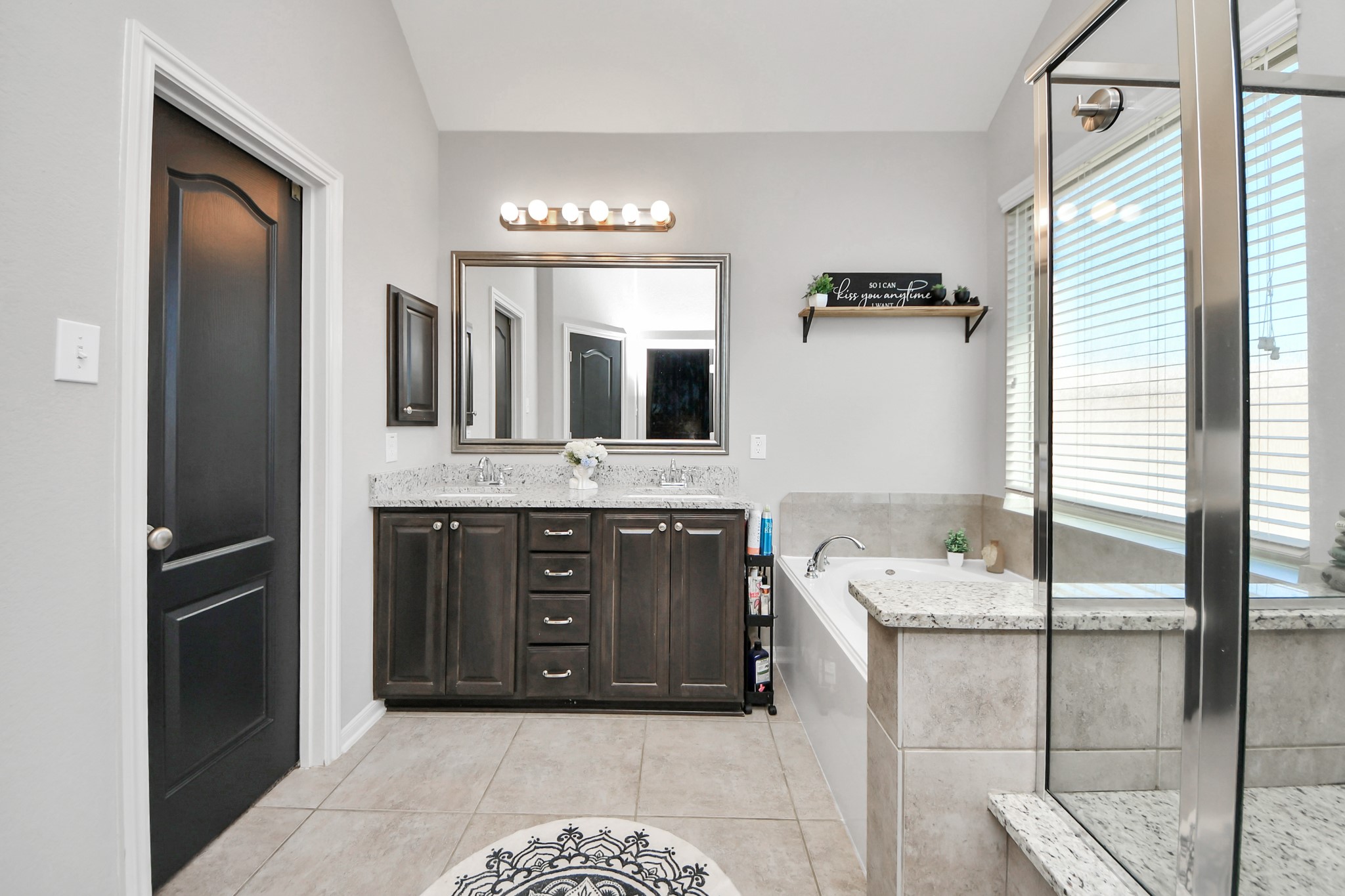 409 Billingsgate Chase, Unit CHASE Conroe, TX 77304 - Photo 21 of 45 The Primary bathroom features a modern design with a granite countertop, dual sinks, and dark wood cabinetry. There's a spacious glass-enclosed shower, a soaking tub, and large window. Neutral tile flooring