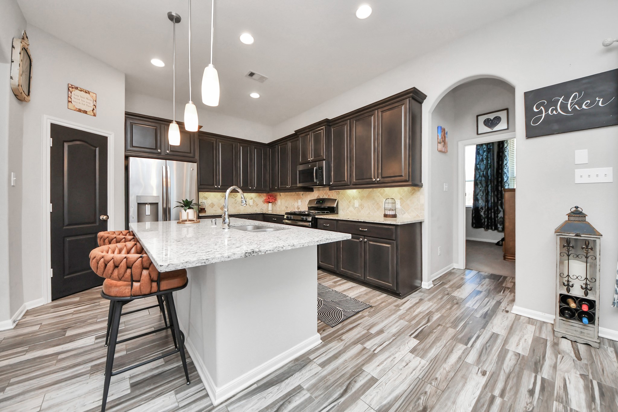 409 Billingsgate Chase, Unit CHASE Conroe, TX 77304 - Photo 6 of 45 This kitchen features modern wood cabinetry, a sleek granite island with seating, stainless steel appliances, and stylish pendant lighting. The open layout and wood-look tile flooring create a warm and inviting atmosphere.