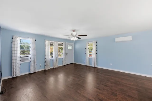 an empty room with wooden floor chandelier fan and windows