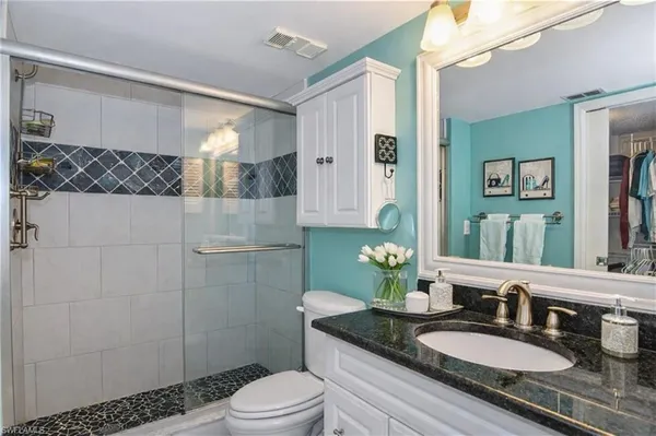 a bathroom with a granite countertop sink a mirror a toilet and shower
