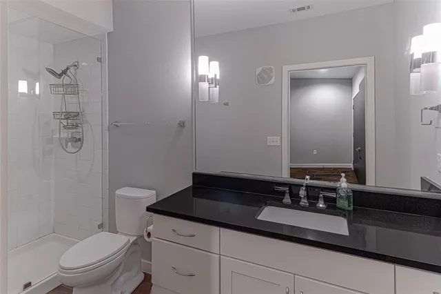 a bathroom with a granite countertop sink a toilet a mirror and shower
