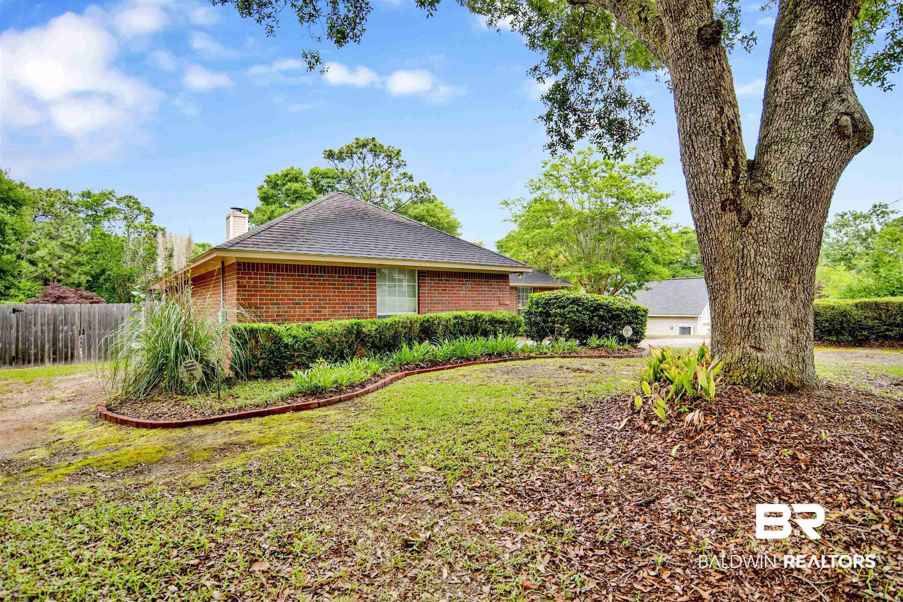 107 Virginia Circle Daphne, AL 36526 - Photo 3 of 47 Brick exterior with a dark shingle roof, surrounded by mature trees and established landscaping beds