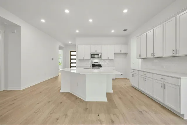a large white kitchen with wooden floor and stainless steel appliances
