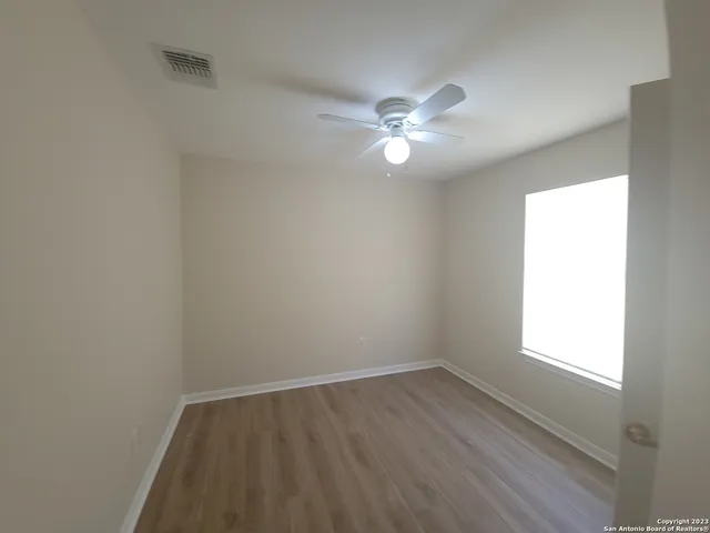 a view of empty room with wooden floor and fan