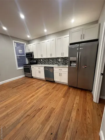 a kitchen with stainless steel appliances granite countertop a refrigerator a sink dishwasher a stove and white countertops with wooden floor