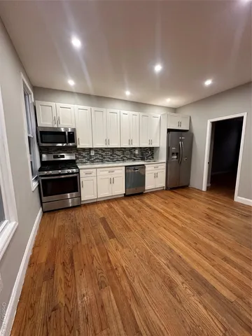 a large kitchen with stainless steel appliances wooden floor and a refrigerator