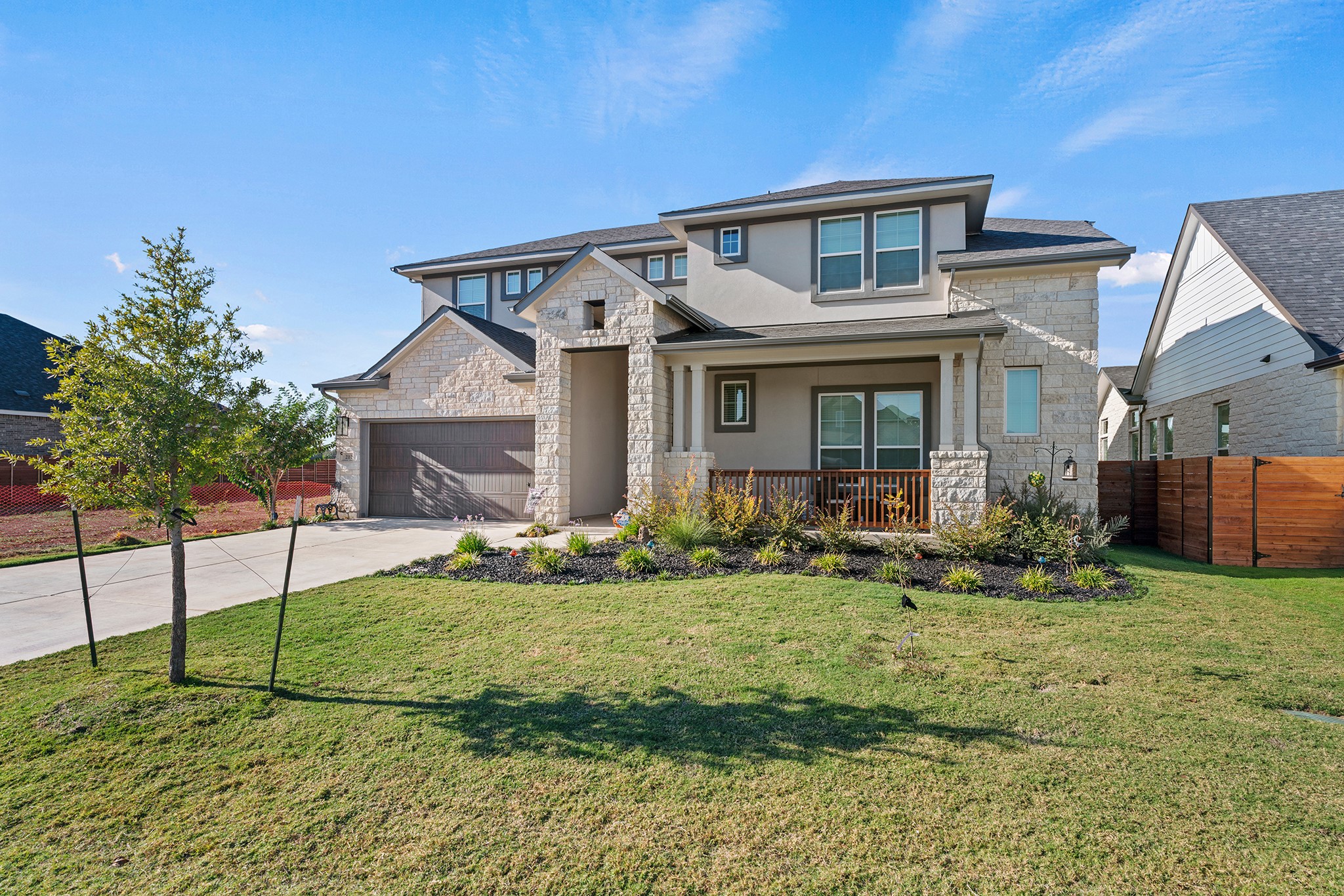 View of front facade with stone siding, driveway, stucco siding, and a porch