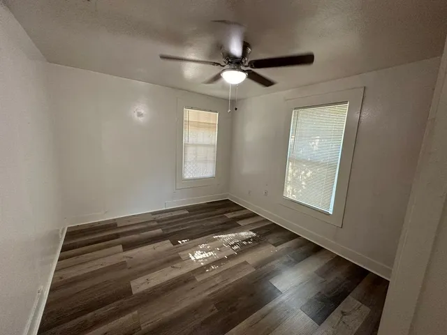 an empty room with wooden floor cabinet and windows