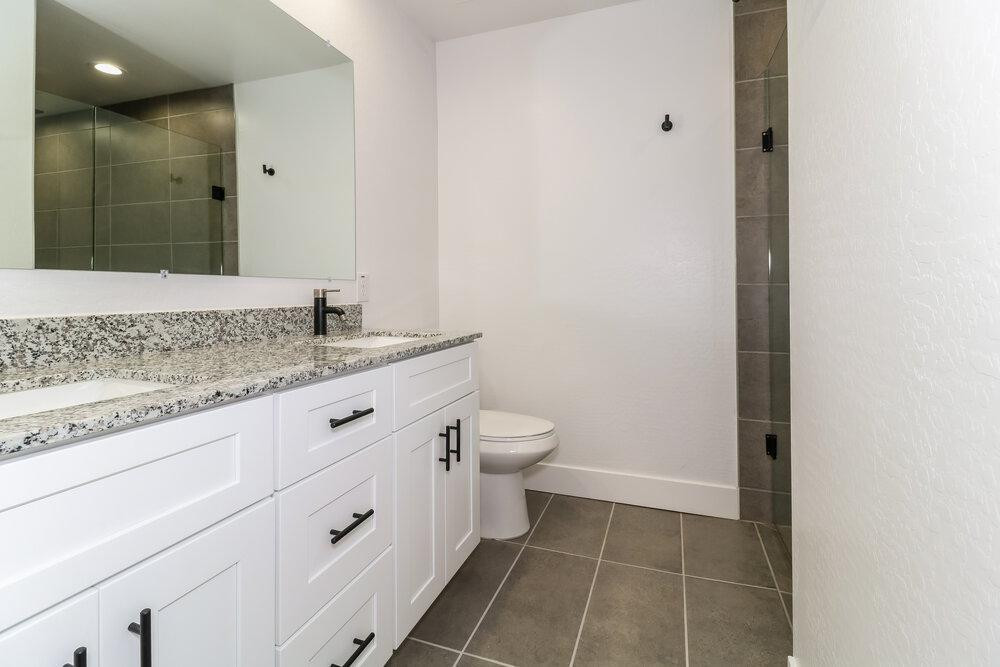 3865 West Gaby Road Phoenix, AZ 85041 - Photo 11 of 16 a bathroom with a granite countertop sink a toilet and a mirror