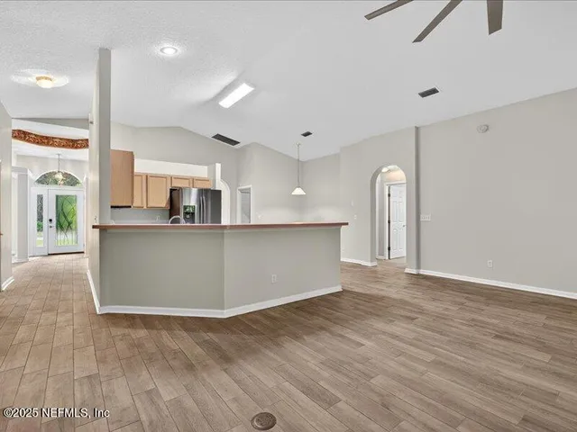 a room with stainless steel appliances kitchen island granite countertop a refrigerator a stove top oven a sink dishwasher and white cabinets with wooden floor