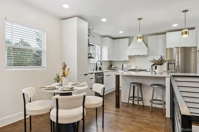 a kitchen with stainless steel appliances granite countertop a stove a refrigerator a kitchen island a dining table and chairs with wooden floor