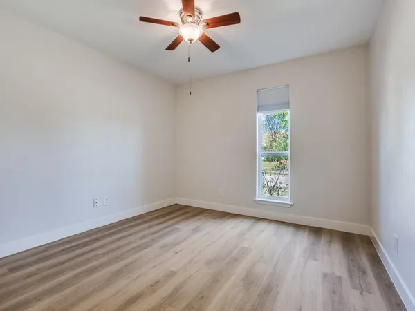 an empty room with wooden floor chandelier fan and windows