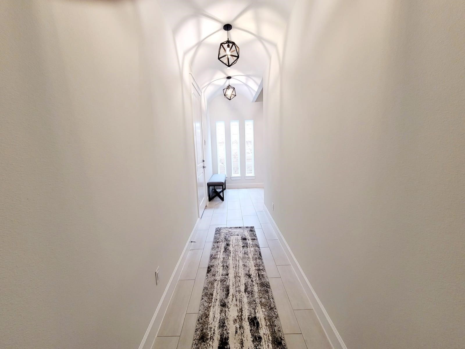 710 Delano Street, Unit A Houston, TX 77003 - Photo 13 of 32 The entry way has a bright, modern hallway with a high ceiling and stylish pendant lights. The space is enhanced by a long rug and natural light streaming through tall windows at the end, creating an inviting entryway.
