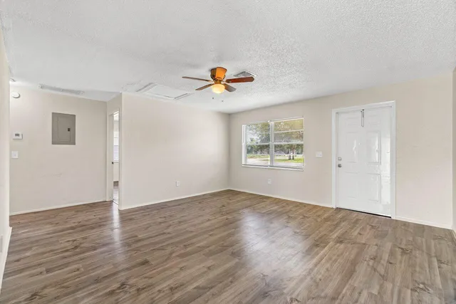 an empty room with wooden floor chandelier fan and windows
