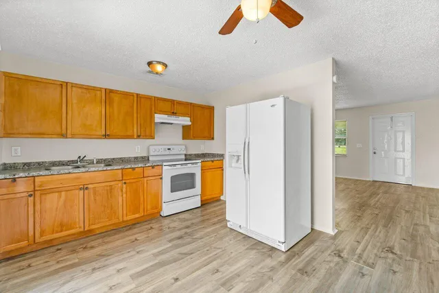 a kitchen with granite countertop wooden floors a stove a sink and a refrigerator