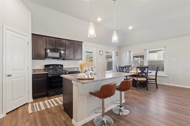 a kitchen with stainless steel appliances granite countertop a stove top oven a sink dishwasher a dining table and chairs with wooden floor